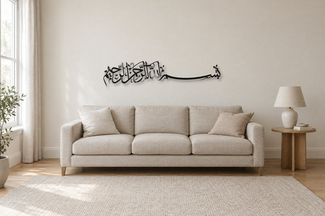 A black metal horizontal Bismillah calligraphy panel, 130 cm wide, hung about 20 cm above a three-seat linen sofa in a light living room