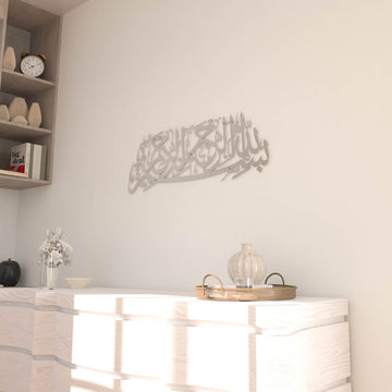 Matte Metall-Wandkunst mit Bismillah in Silber, an einer Wand neben einem Eckregal