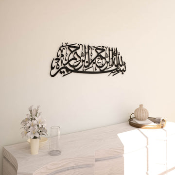 Matte Metall-Wandkunst mit Bismillah in Schwarz, an einer cremefarbenen Wand, Vorderansicht mit Lilienvase darunter