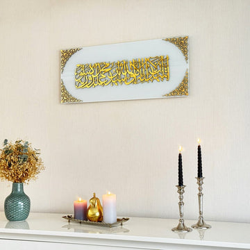 Kalima-Shahada-Glaskunst in goldenem Acryl auf einfarbig weißem Glas über einem weißen Sideboard, Ansicht mit Kerzenständern
