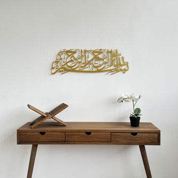 Matte Metall-Wandkunst mit Bismillah in Gold, über einem hölzernen Konsolentisch mit Koranständer