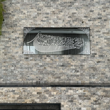 لوحة زجاج مرآة أسود بالاستعاذة والبسملة بخط أكريليك فضي على جدار حجري، منظر مستقيم