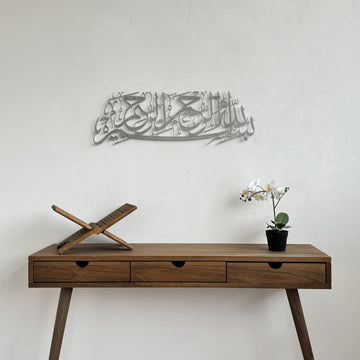 Matte Metall-Wandkunst mit Bismillah in Silber, über einem hölzernen Konsolentisch mit Koranständer