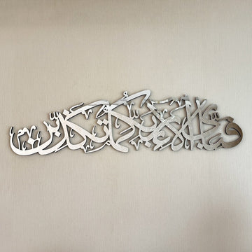 Close-up of the silver acrylic Ar-Rahman 13th verse calligraphy on a textured wall