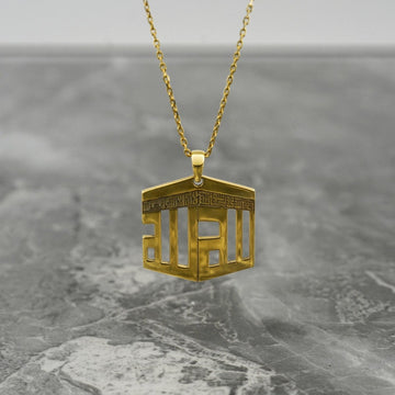 Collier pendentif Kaaba doré suspendu au-dessus d'une surface en marbre gris