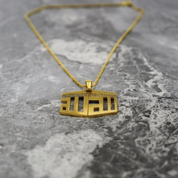 Collier pendentif Kaaba doré avec une chaîne plus épaisse posé sur du marbre gris