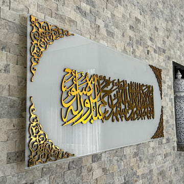 Nahe Schrägansicht der Kalima-Shahada-Kalligraphie in goldenem Acryl auf einfarbig weißem Glas mit Eckornamenten