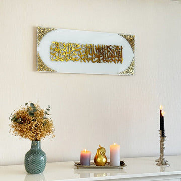 Kalima-Shahada-Glaskunst in goldenem Acryl auf einfarbig weißem Glas über einem weißen Sideboard, Ansicht mit Vase und Kerzen