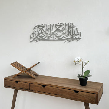 Matte Metall-Wandkunst mit Bismillah in Silber, an einer weißen Wand, nähere Ansicht über einer Holzkonsole