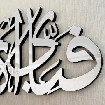 Extreme close-up of silver mirror acrylic letters over a black wooden layer on the Ar-Rahman verse art