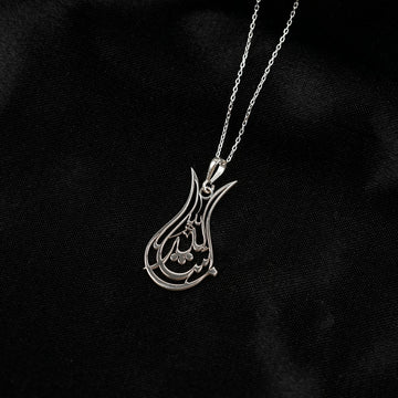 Silver Tulip Mashallah necklace hanging against black fabric, openwork tulip outline