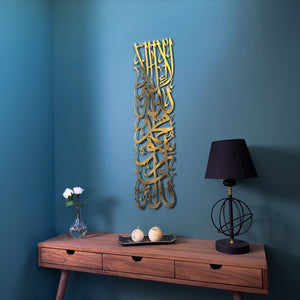 Art mural vertical en métal Première Kalima doré brillant sur un mur bleu canard au-dessus d'une console en bois et d'une lampe