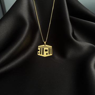 Collier pendentif Kaaba doré suspendu à une chaîne fine au-dessus de satin noir, vue éloignée
