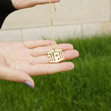 Collier pendentif Kaaba doré dans une main ouverte, en extérieur sur l'herbe