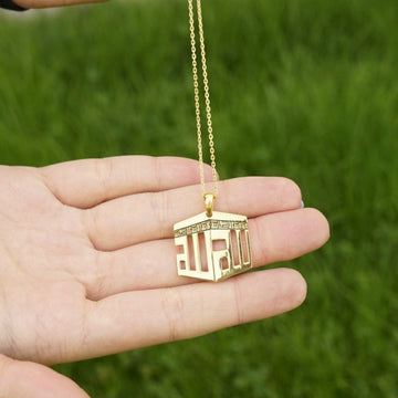 Collier pendentif Kaaba doré posé sur une paume ouverte, comparaison d'échelle avec une main