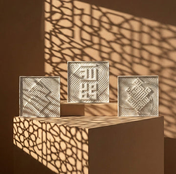 Ensemble de trois carreaux coufiques en relief à différentes hauteurs sur un bloc, sous une lumière du soleil à motifs