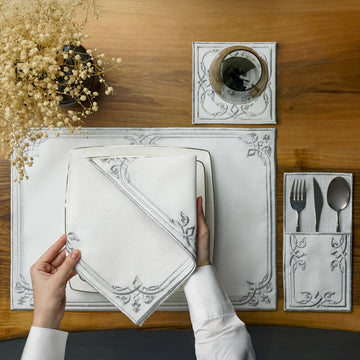 Silver interlocking scroll border placemat with napkin on a square plate, overhead view with hands