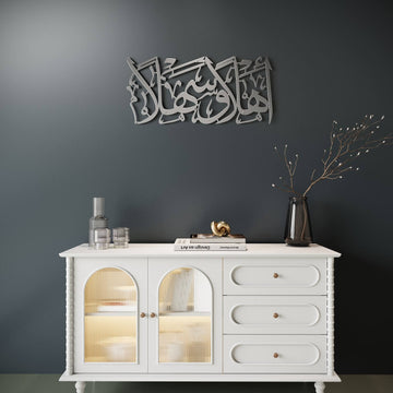 Silberne Ahlan wa Sahlan Metall-Wandkunst mittig über einem weißen Sideboard an dunkelgrauer Wand