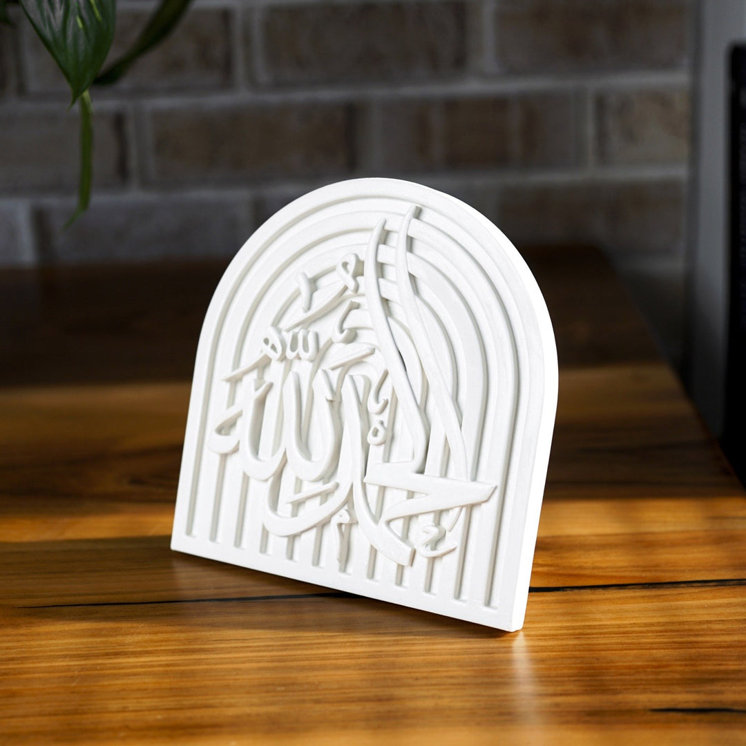 Alhamdulillah stone relief arch plaque angled on a wooden table by a brick wall