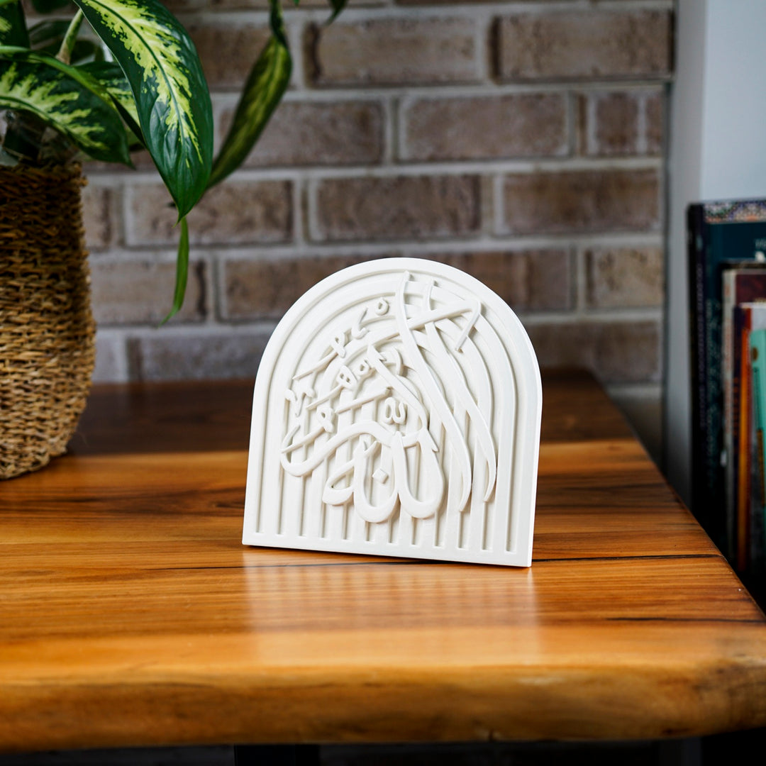 Small Allah-u Akbar stone arch plaque on a wooden side table beside a brick wall