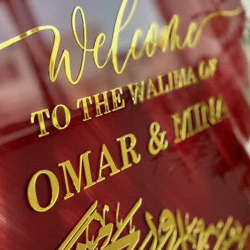 Close-up of raised gold Welcome to the Walima lettering and Arabic calligraphy on the red glass sign