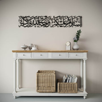 Art mural en métal noir As-Salamu Alaykum sur un mur clair, vue large montrant la console et les paniers en dessous