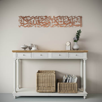 Art mural en métal As-Salamu Alaykum cuivré mat sur un mur clair, vue large au-dessus d'une console et de paniers