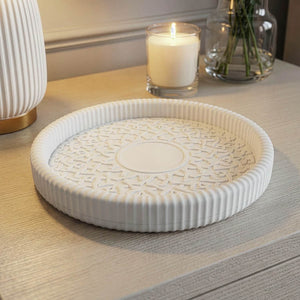 White cast stone Aslam Al Silahdar medallion catchall tray with ribbed rim, on a console beside a candle