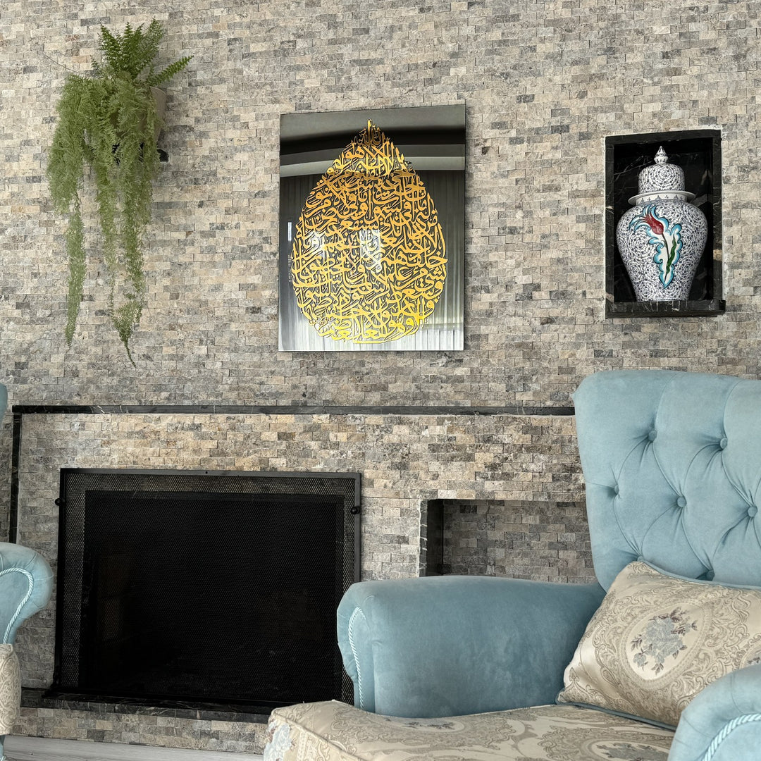 Art mural en verre Ayatul Kursi en forme de goutte, doré, sur un mur en pierre au-dessus d'une cheminée et d'un fauteuil bleu