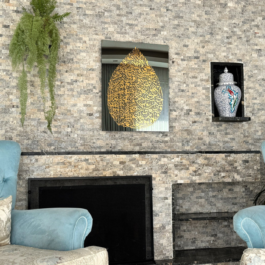 Art mural en verre Ayatul Kursi en forme de goutte, doré, vue large au-dessus d'une cheminée avec une plante suspendue