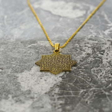 Close-up of the gold octagonal Ayatul Kursi pendant on a chain over gray marble