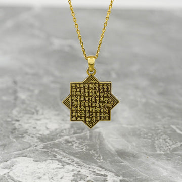 Gold octagonal Ayatul Kursi necklace hanging against a gray marble surface