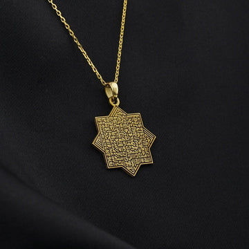 Gold octagonal Ayatul Kursi pendant seen at a slight angle against black fabric