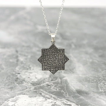 Silver octagonal Ayatul Kursi necklace hanging against a gray marble surface
