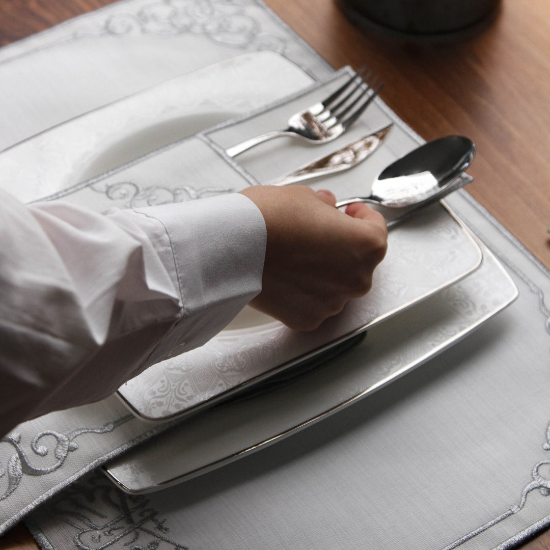 Silver embroidered Basmala placemat and cutlery pouch set on a table with hand holding a spoon