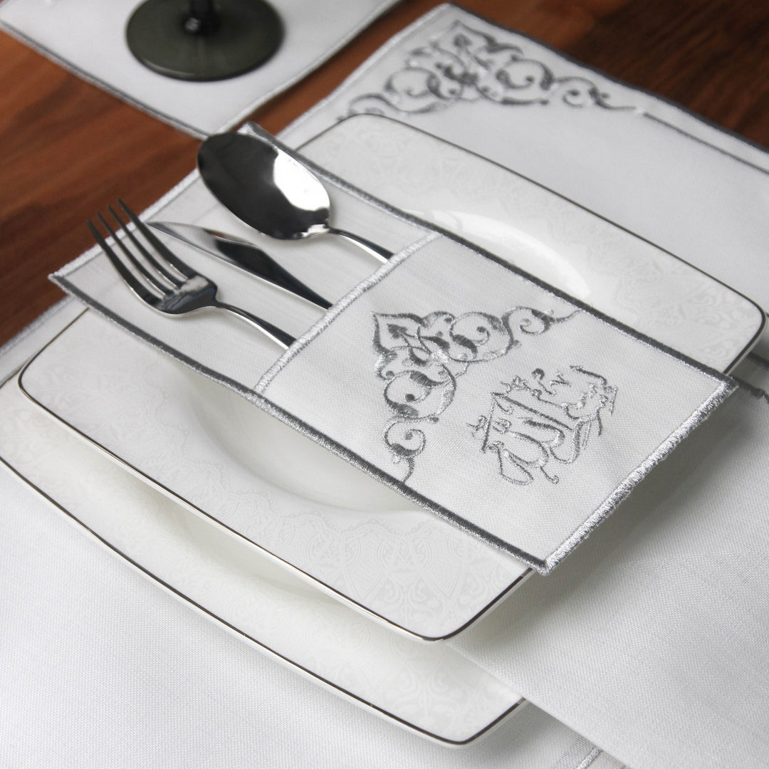 Silver embroidered Basmala cutlery pouch with silverware resting beside a white plate