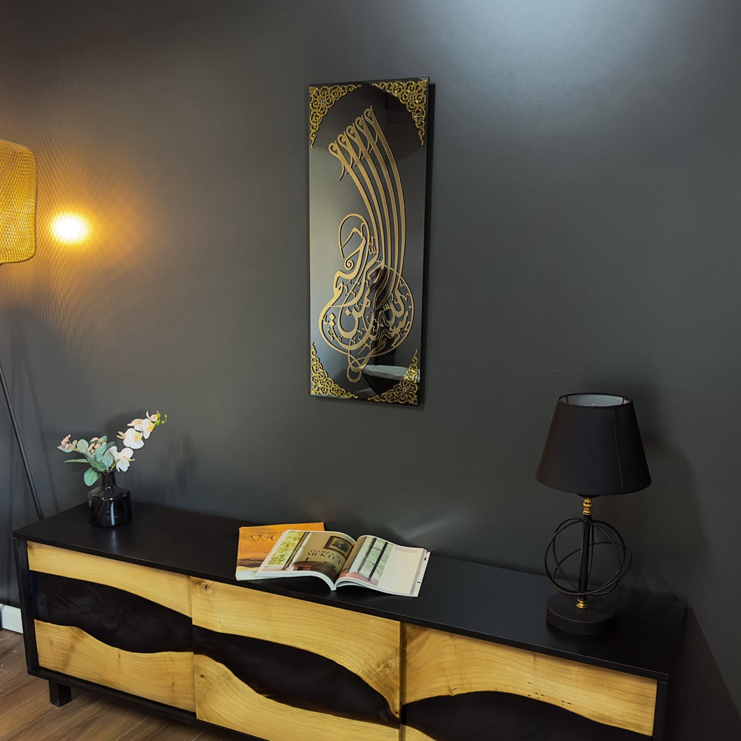 Art mural en verre Bismillah à calligraphie dorée, vue en biais sur un mur sombre au-dessus d'une console et d'une lampe