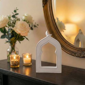 Small stone mihrab arch with crescent moon beside lit candles on a dark console
