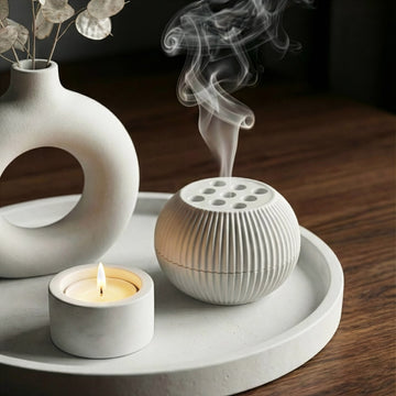 White ceramic diffuser with smoke, candle, and vase on a wooden surface