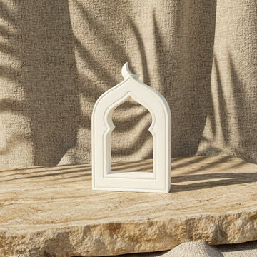White mihrab stone arch on a travertine slab against a draped linen backdrop with palm shadows