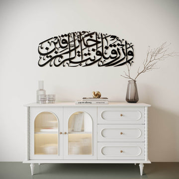 Art mural en métal noir Dua pour le rizq, plus petit dans le cadre, au-dessus d'un meuble blanc à portes vitrées