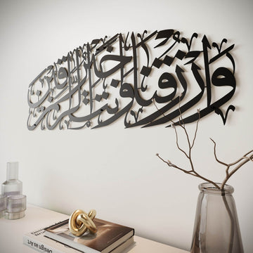 Art mural en métal noir Dua pour le rizq, vue en angle rapprochée avec un vase, une branche et un objet déco en dessous