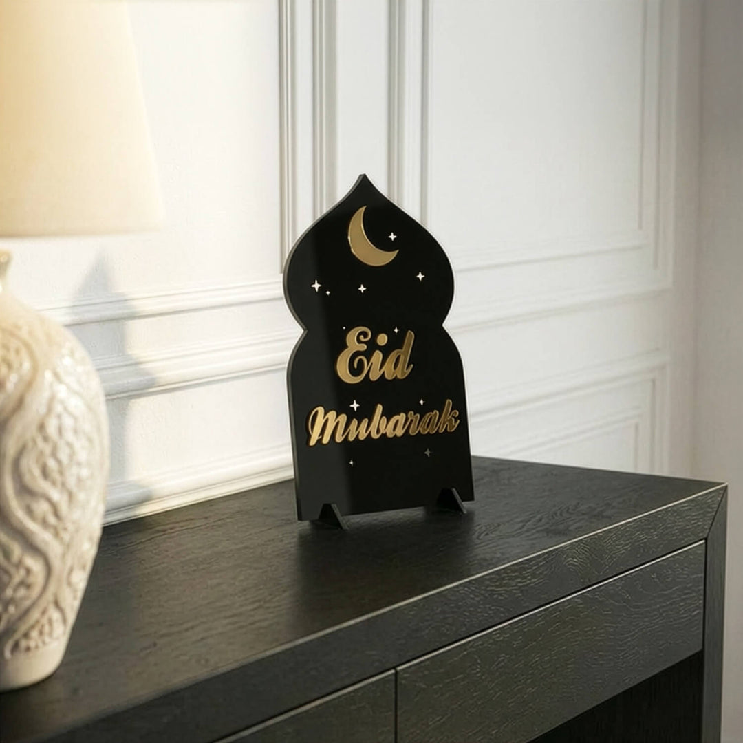 Eid-Mubarak-Acrylaufsteller in Gold auf Schwarz aus größerer Entfernung auf einer schwarzen Konsole
