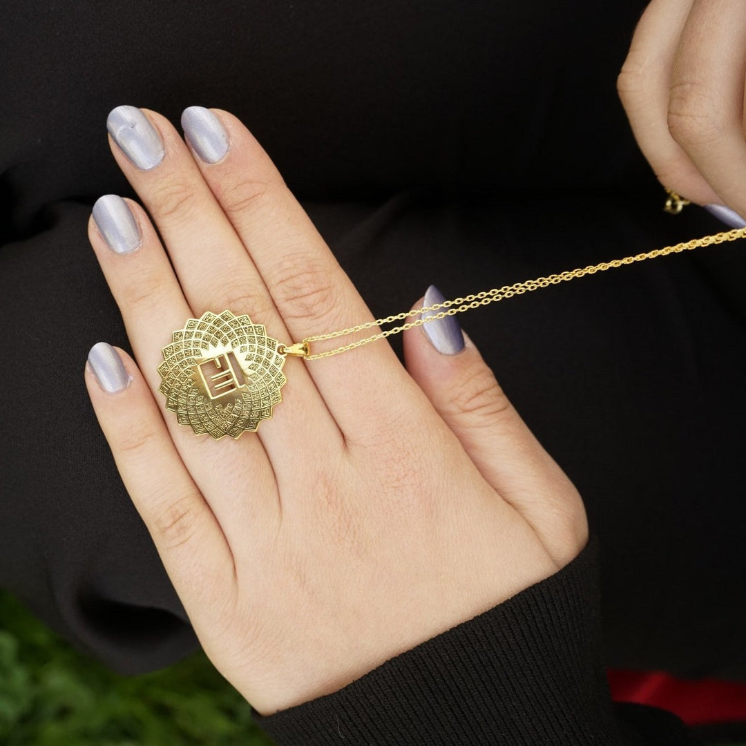 Hand hält den goldenen Asma-ul Husna Anhänger zwischen den Fingern, um seine Größe zu zeigen