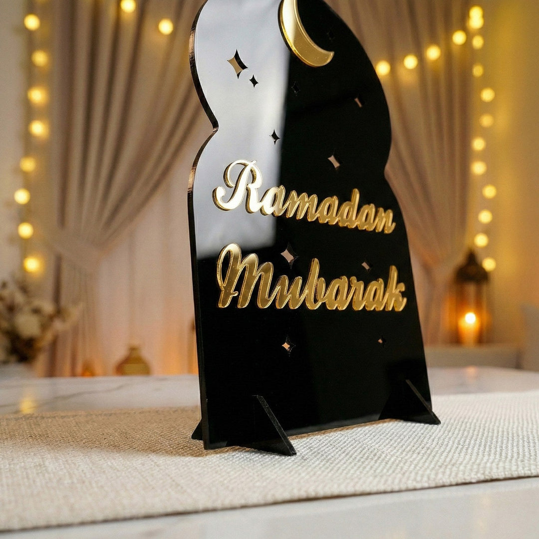 Schräge Nahansicht des Ramadan-Mubarak-Acrylaufstellers in Schrift-Design, Gold auf Schwarz, und seines Sockels