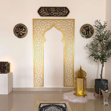 Gold metal mihrab with Allah and Muhammad calligraphy and Surah Al-Baqarah 2:144 plaque in a prayer corner