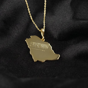 Gold Saudi Arabia map necklace with the Shahada and sword engraved on the pendant, on black fabric