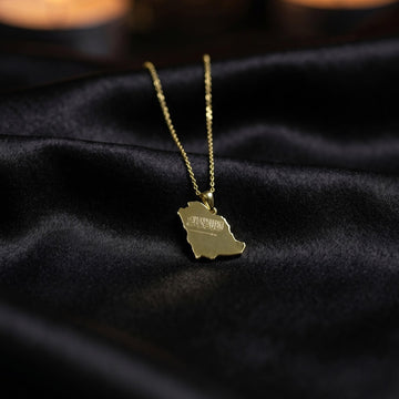 Small gold Saudi Arabia map pendant on a thin chain, draped over black satin