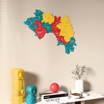 Flag colored Guinea wooden wall map on a beige wall above a console with figurines