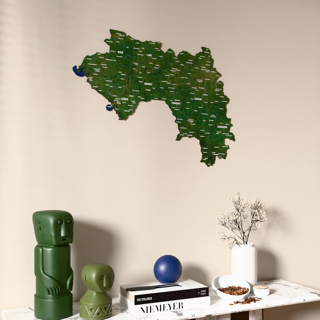 Satellite Guinea wooden wall map on a beige wall above a console with figurines
